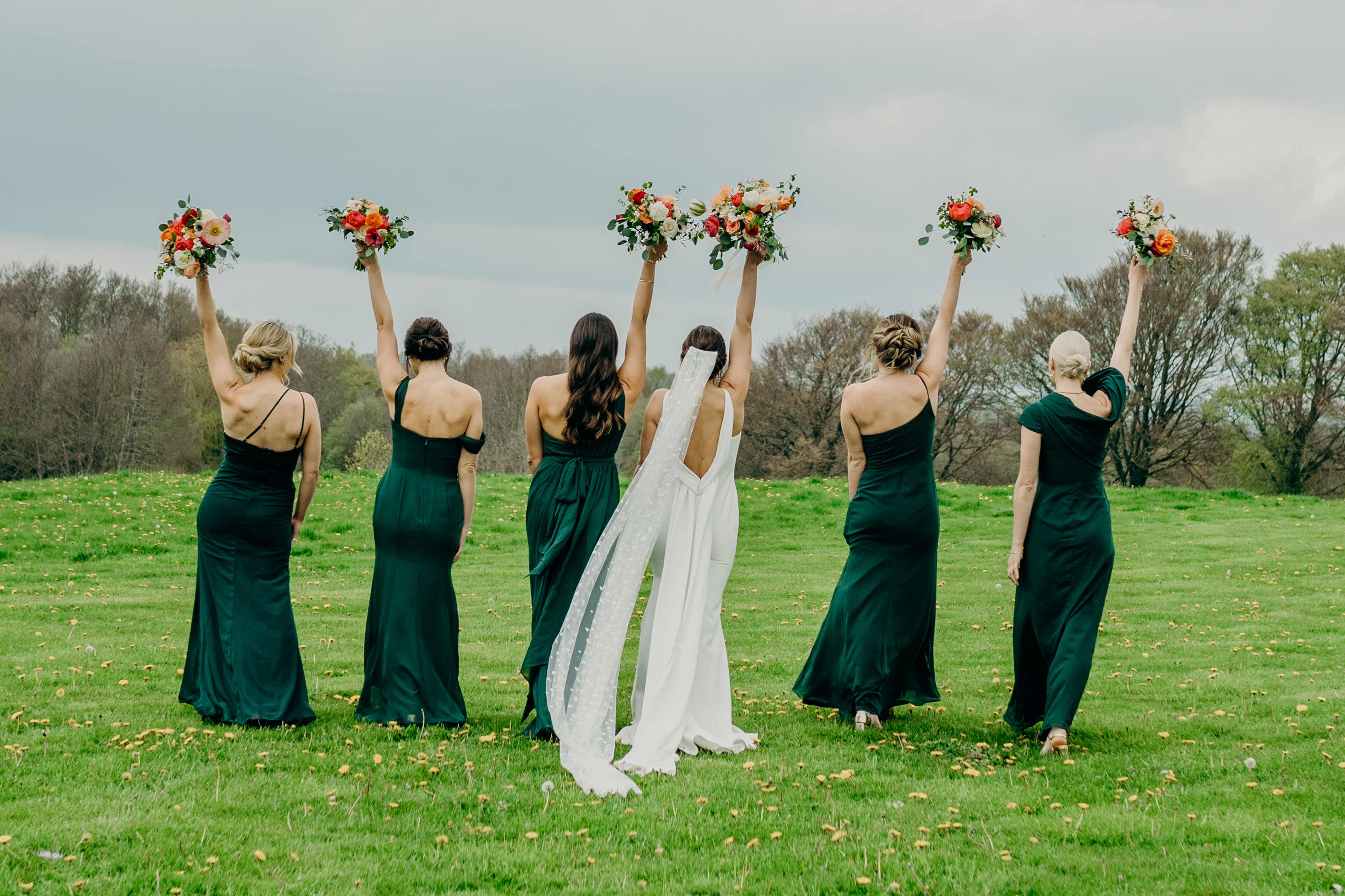 Bride and bridesmaids in a field holding bouquets overhead